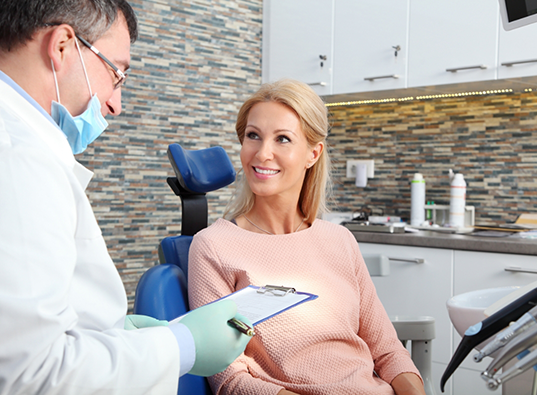 Woman in dental chair listening as her dentist reads from a clipboard