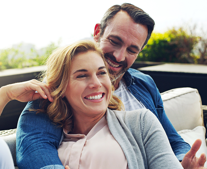 Man and woman sitting on outdoor couch and smiling after cosmetic dentistry in Raleigh