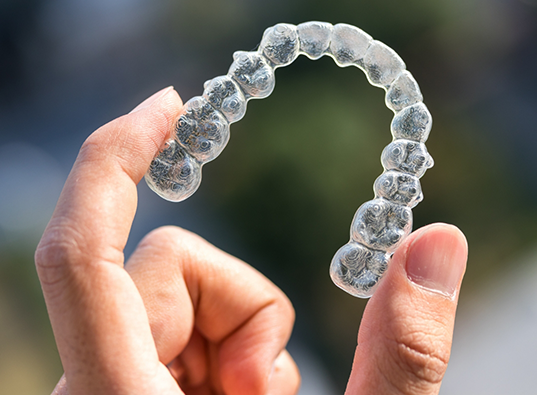 Hand holding an Invisalign clear aligner