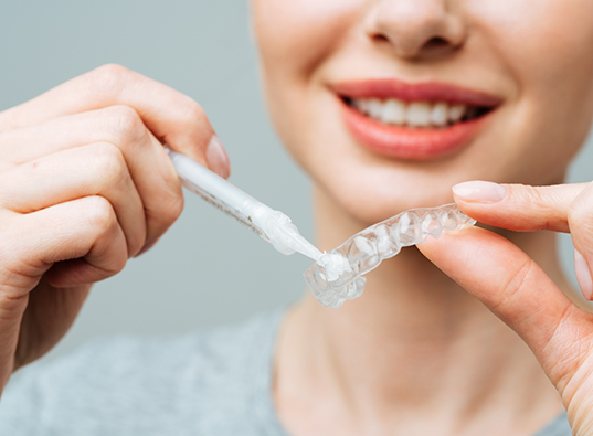 Person putting teeth whitening gel into a tray to be worn over the teeth