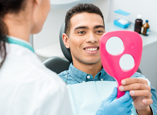 Man in dental chair looking at his smile in a mirror