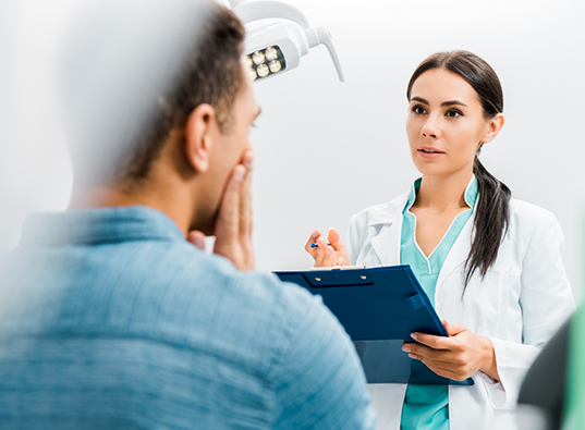 Dentist holding a clipboard while talking to a patient in the treatment chair