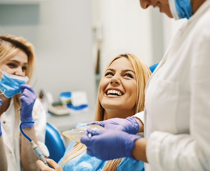 Woman in dental chair grinning up at her dentist