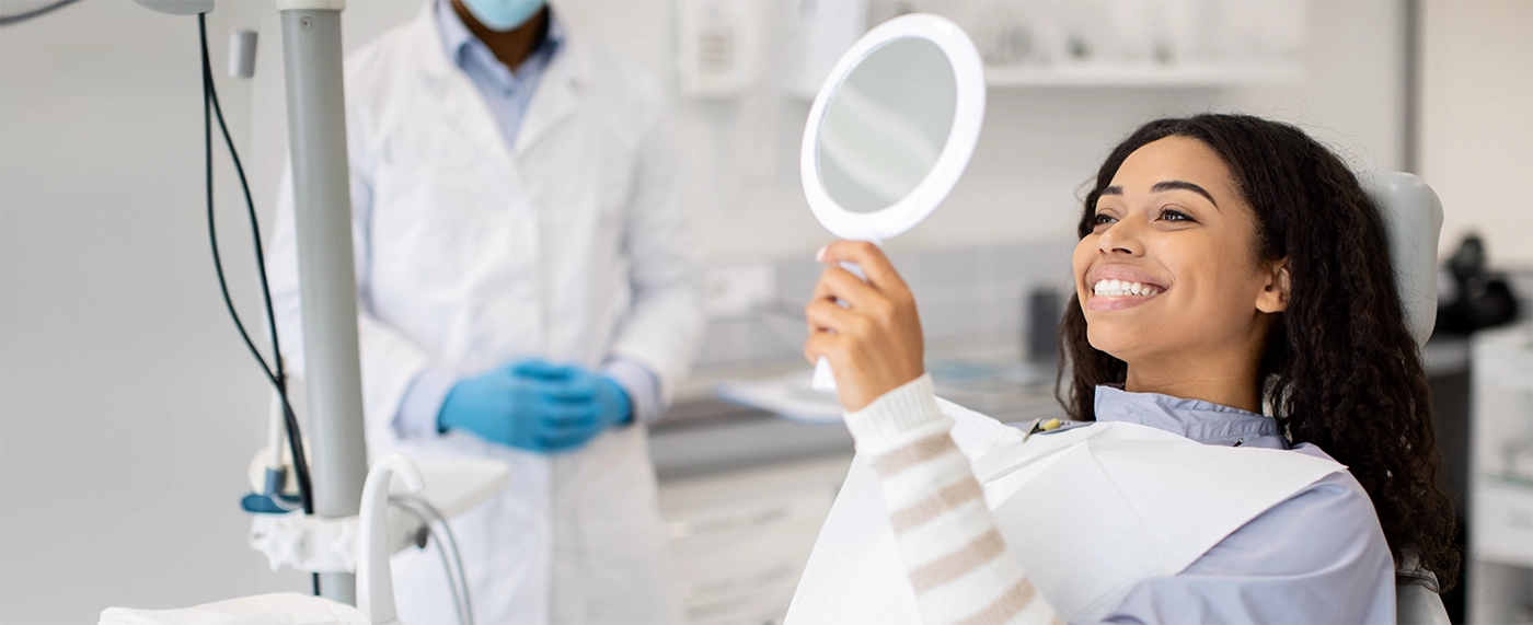 Young woman in dental chair holding a mirror and beaming at her new smile