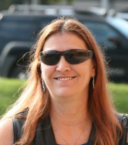 Woman with long dark red hair and sunglasses smiling outdoors