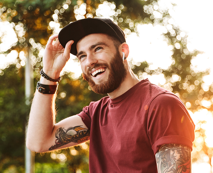 Young man with arm tattoos smiling outdoors after treatment with Invisalign in Raleigh