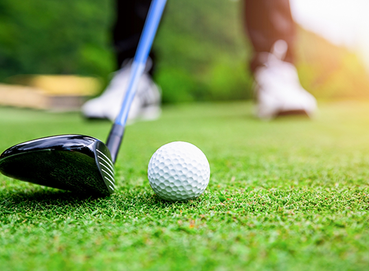 Person lining up their golf club to a golf ball on the ground