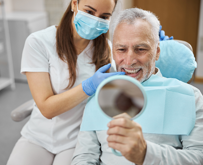 Senior dental patient looking at his smile in mirror after replacing missing teeth