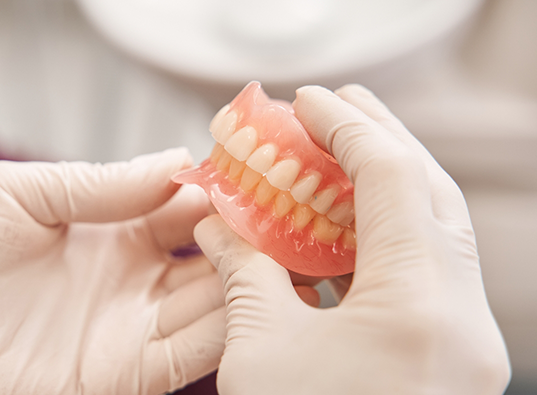 Two gloved hands holding a set of full dentures