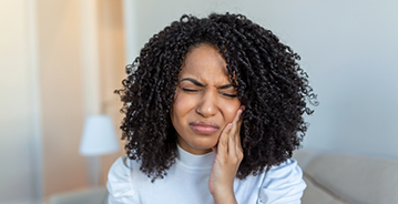 Woman wincing in pain and holding the side of her jaw