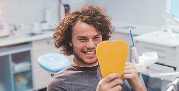 Young man in dental chair looking at his smile in a mirror