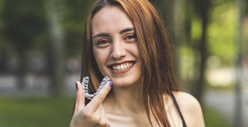 Young woman smiling and holding an Invisalign clear aligner