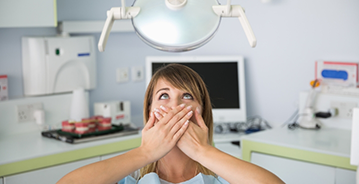 Nervous woman in dental chair covering her mouth in fear