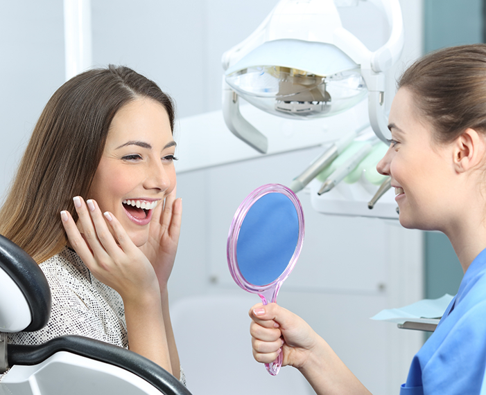 Woman admiring her new smile in a mirror after restorative dentistry in Raleigh