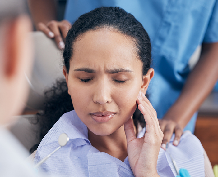 Woman in dental chair holding her cheek in pain before root canal treatment