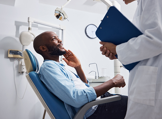 Man smiling and touching his face while talking to his dentist