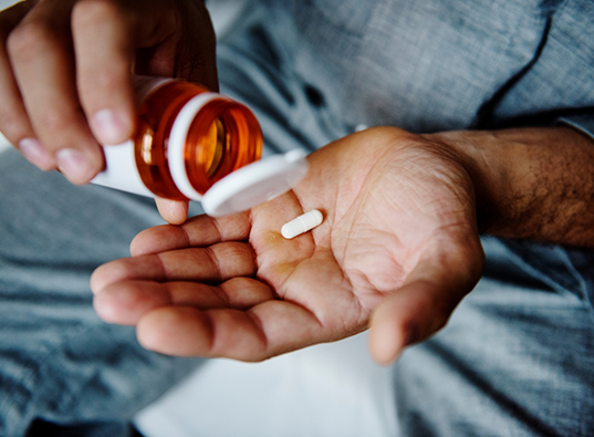 Person pouring a white pill out of an orange bottle and into their hand